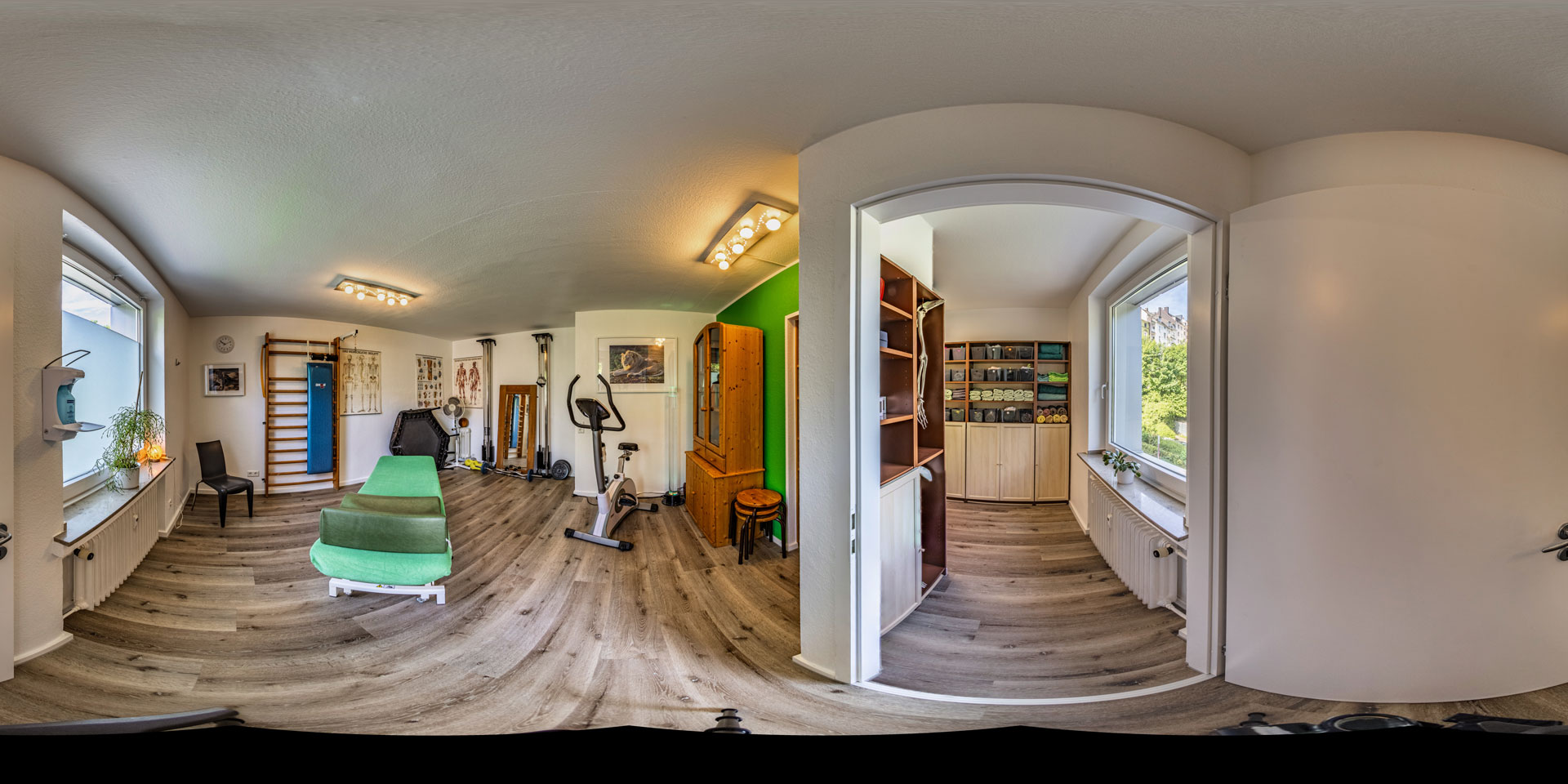 Panorama einer modernen Praxis mit Sportgeräten, grüner Liege und hellen Wänden.
