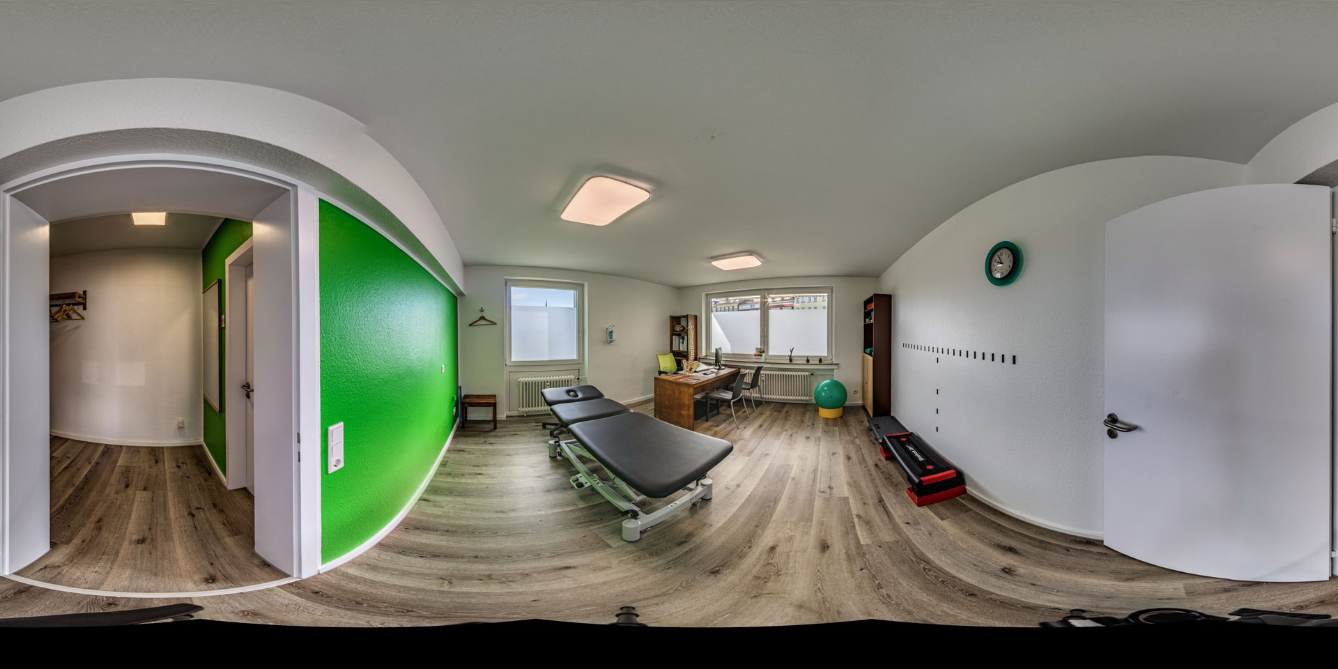 Panorama eines modernen Physiotherapieraums mit grüner Akzentwand und Behandlungsliege.