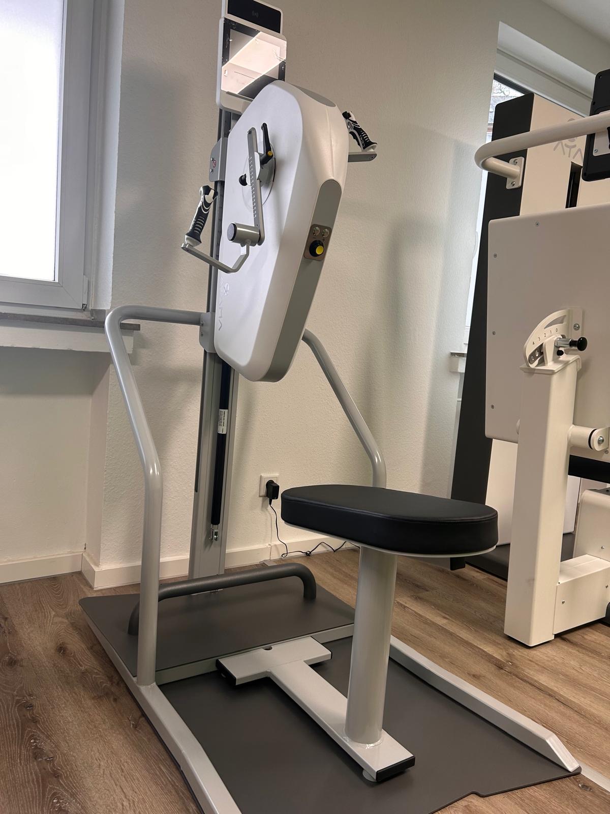Ein weißes Fitnessgerät mit Sitzfläche steht in einem hellen Raum mit Holzfußboden