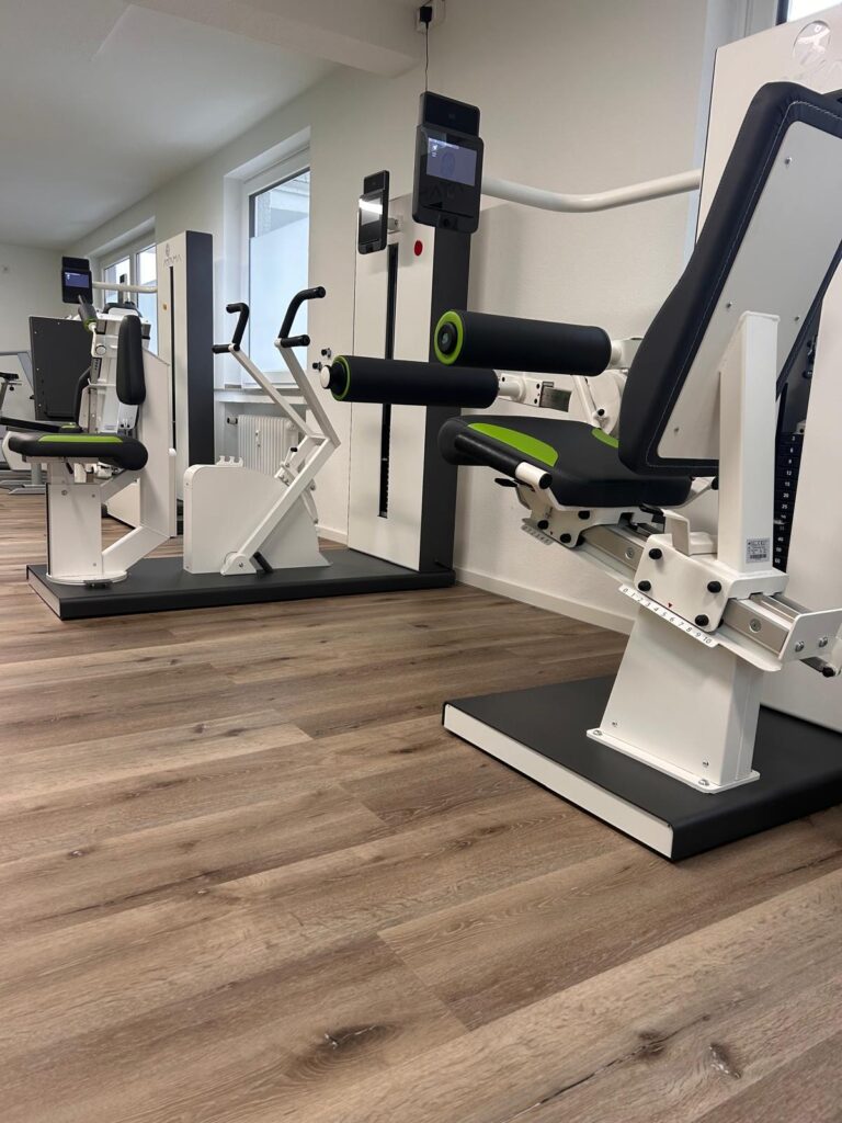 Helles Fitnessstudio mit modernen weissen Trainingsgeraeten und hellbraunem Holzfussboden