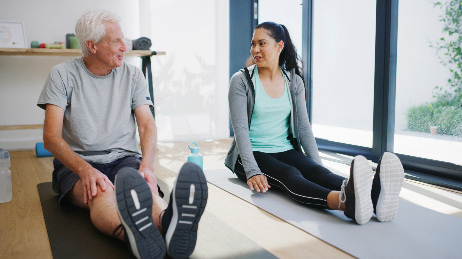 Physiotherapie, Yoga und alter Mann im Studio mit Hilfe, Checkup und Workout in der Rehabilitation. Gesundheitspflege, Unterstützung oder Trainer im Fitnessstudio mit Übungsmatte, Verletzungsrückgewinnung oder Prävention im Ruhestand.