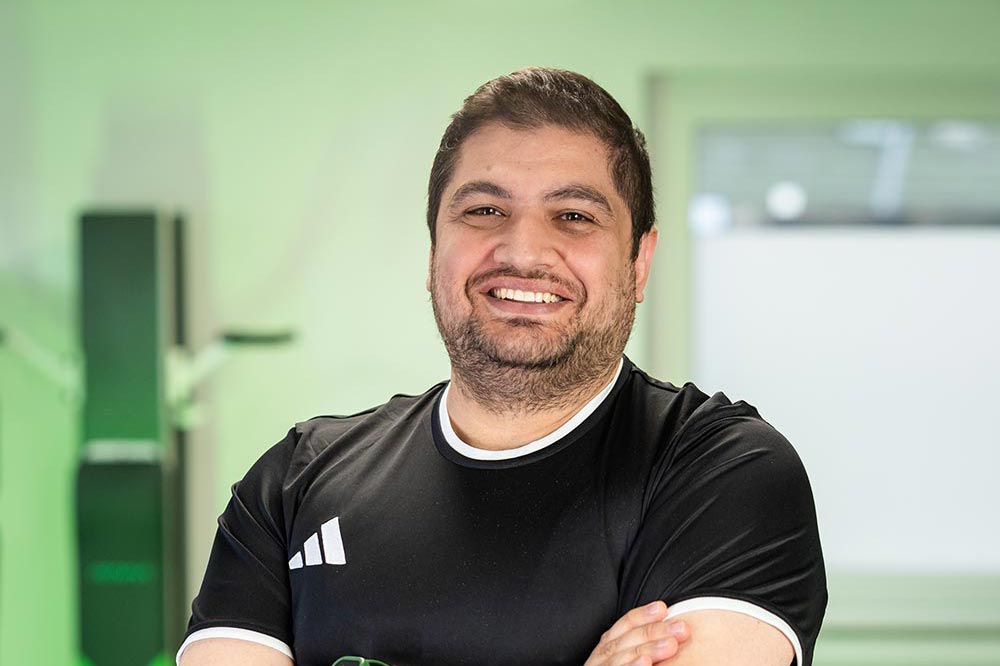 Mann mit neutralem Ausdruck in schwarzem Shirt mit Armen verschraenkt
