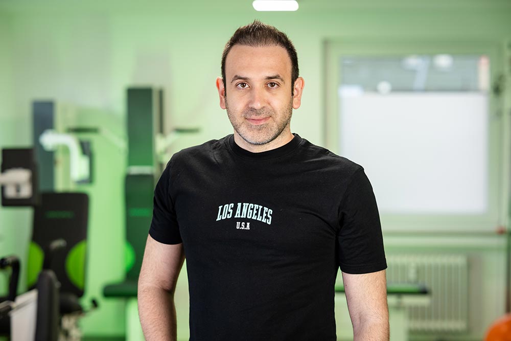 Mann mit neutralem Blick im schwarzen Los Angeles Shirt im gruenen Fitnessraum